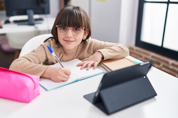 Adorable hispanic girl student sitting on table studying at classroom