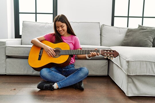 Young latin woman playing classical guitar sitting on floor at home