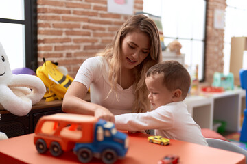 Teacher and toddler playing with cars toy sitting on table at kindergarten