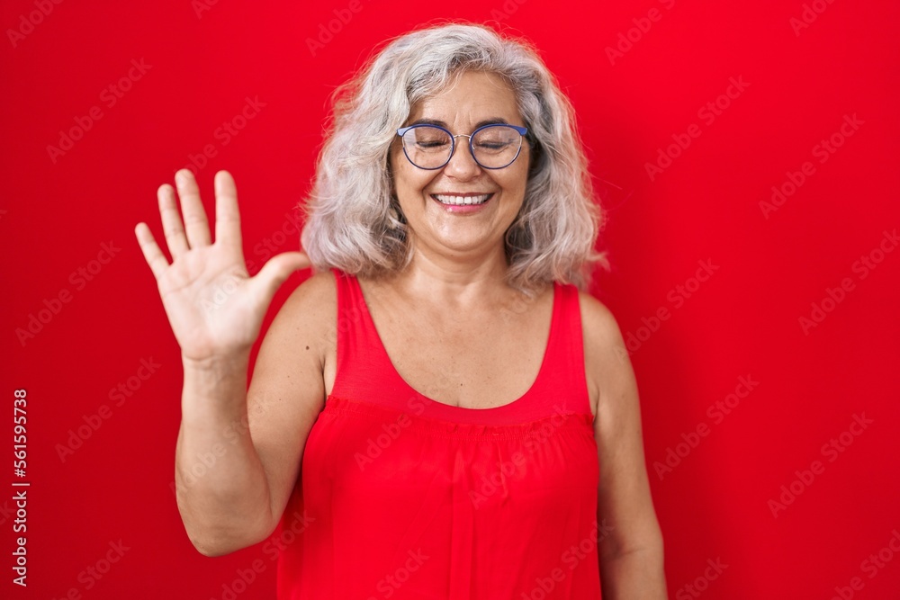 Poster middle age woman with grey hair standing over red background showing and pointing up with fingers nu