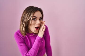 Hispanic woman standing over pink background hand on mouth telling secret rumor, whispering malicious talk conversation