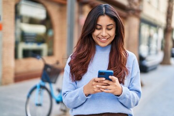 Young hispanic woman smiling confident using smartphone at street