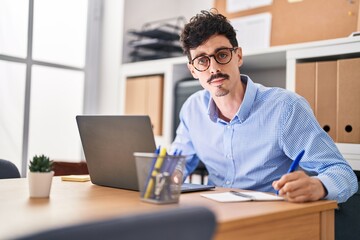 Young caucasian man business worker using laptop writing on notebook at office