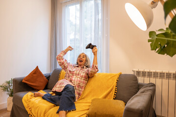Obraz premium old woman plays console at home. celebrate a victory in online video games