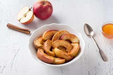 A white bowl of baked apple slices with cinnamon on a light blue background. Delicious homemade vegan dessert