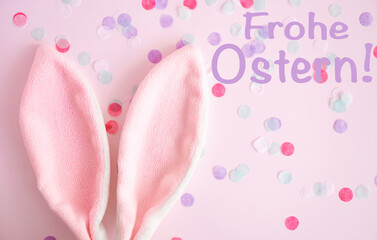 Easter greeting card .Pink bunny ears on pink pastel background wint confetti with text Frohe .Ostern . Easter minimal concept. flat lay