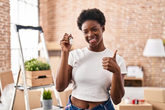 African american woman holding keys of new home smiling happy and positive, thumb up doing excellent and approval sign