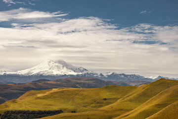 Big mountain Elbrus against the blue sky. View from a large plateau and steep cliffs.