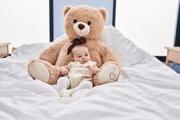 Adorable baby relaxed lying on bed with teddy bear at bedroom