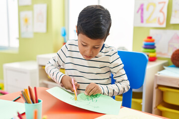 Adorable hispanic boy student cutting paper at kindergarten