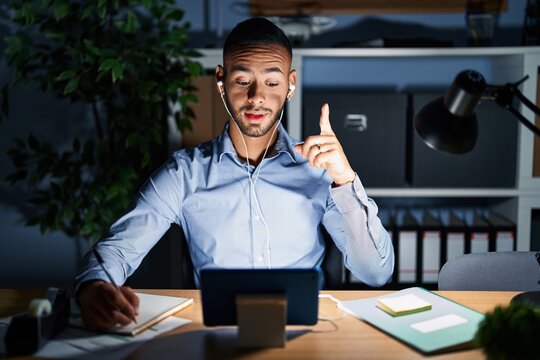 Young hispanic man working at the office at night pointing finger up with successful idea. exited and happy. number one.