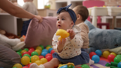 Two toddlers playing with toys sitting on floor at kindergarten