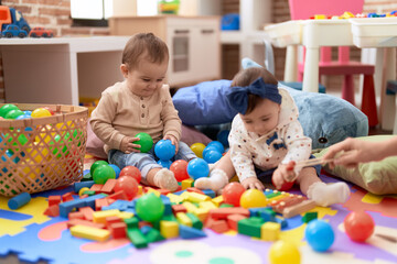 Two toddlers playing with balls and xylophone sitting on floor at kindergarten