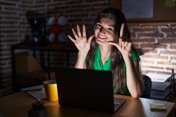 Young teenager girl working at the office at night showing and pointing up with fingers number seven while smiling confident and happy.