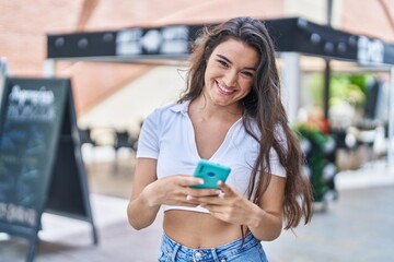 Young hispanic woman smiling confident using smartphone at street