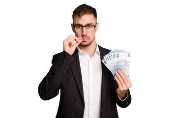 Young business caucasian man holding euro banknotes isolated cut out with fingers on lips keeping a secret.