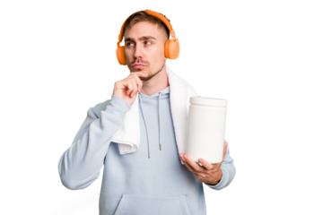 Young fitness man listening to music and holding a protein bottle isolated cut out looking sideways with doubtful and skeptical expression.