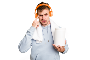 Young fitness man listening to music and holding a protein bottle isolated cut out showing a disappointment gesture with forefinger.