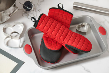 Oven mitts lying in a baking pan surrounded by kitchen utensils