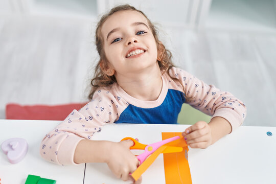 Adorable blonde girl student smiling confident cutting paper at kindergarten