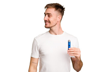 Young caucasian man holding a vaporizer cut out isolated looks aside smiling, cheerful and pleasant.