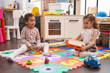 Two kids playing xylophone sitting on floor at kindergarten