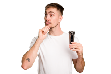 Young man holding a shaving machine cut out isolated looking sideways with doubtful and skeptical expression.