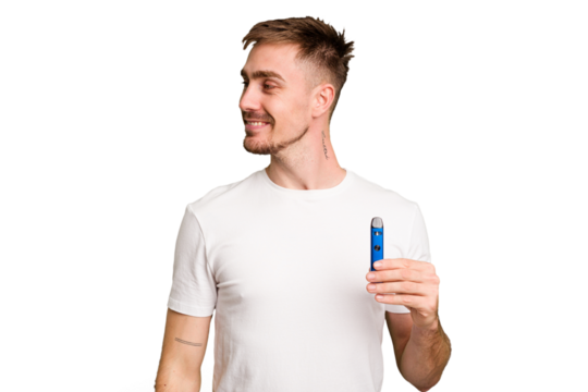 Young caucasian man holding a vaporizer cut out isolated looks aside smiling, cheerful and pleasant.
