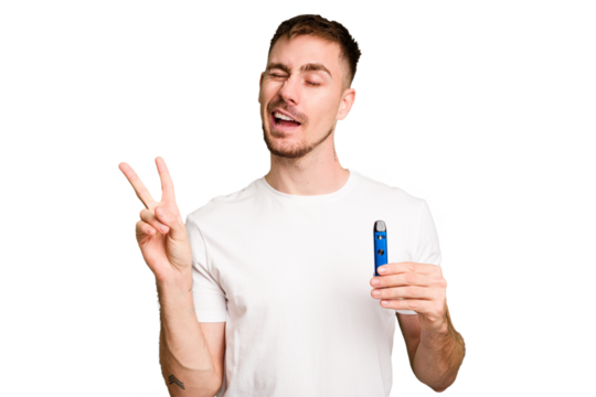 Young caucasian man holding a vaporizer cut out isolated joyful and carefree showing a peace symbol with fingers.