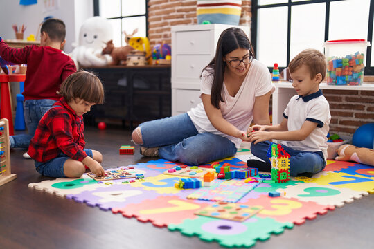Teacher with boys playing with maths puzzle game sitting on floor at kindergarten