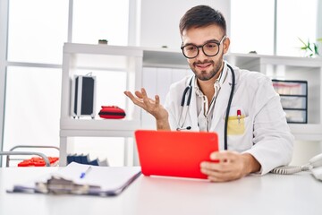 Young hispanic man doctor using touchpad having video call at clinic