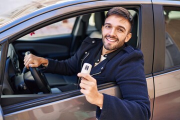 Young hispanic man smiling confident holding key of new car at street