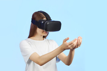 Young teen girl in a virtual reality helmet isolated on a blue background is holds a three-dimensional object in her hands and looks at it.