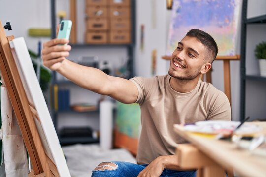 Young hispanic man artist making selfie by the smartphone at art studio