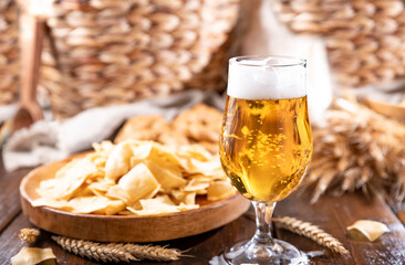 Glass of light craft beer on a wooden table. Beer is poured into a glass with foam and bubbles. for social media. beer texture. On a plate are bread chips traditional in Italy on Sardinia