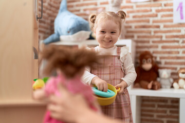 Fototapeta premium Adorable caucasian girl playing with play kitchen standing at kindergarten