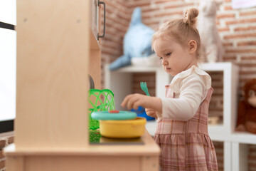 Adorable caucasian girl playing with play kitchen standing at kindergarten
