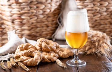 Pouring beer into the glass. Wheat spikelets with one mugs of beer on wooden background. Cold lager beer. Craft beer forms waves. Freshness and foam.Nearby are Neapolitan taralli from Italy.