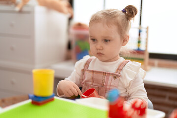 Adorable caucasian girl playing with play kitchen sitting on table at kindergarten