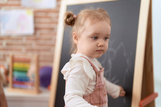 Adorable caucasian girl drawing on blackboard standing at kindergarten