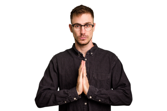 Young caucasian man cut out isolated praying, showing devotion, religious person looking for divine inspiration.