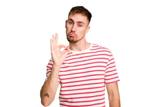 Young caucasian man cut out isolated winks an eye and holds an okay gesture with hand.
