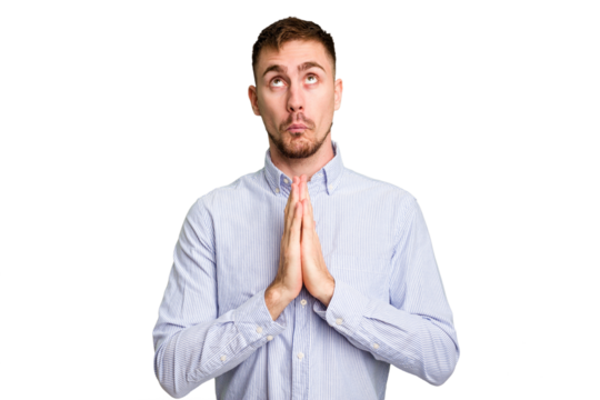 Young caucasian man cut out isolated holding hands in pray near mouth, feels confident.