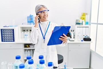 Middle age grey-haired woman wearing scientist uniform talking on the smartphone at laboratory