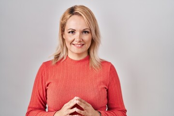 Fototapeta premium Blonde woman standing over isolated background hands together and fingers crossed smiling relaxed and cheerful. success and optimistic