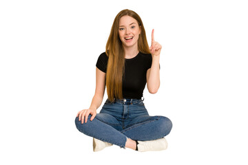 Young redhead woman sitting on the floor cut out isolated showing number one with finger.