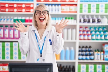 Young caucasian woman working at pharmacy drugstore celebrating crazy and amazed for success with arms raised and open eyes screaming excited. winner concept