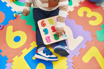 Adorable hispanic toddler playing with maths puzzle game sitting on floor at kindergarten