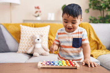 Adorable hispanic toddler playing xylophone standing at home