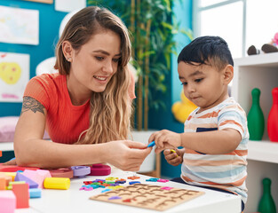 Teacher and toddler playing with maths puzzle game sitting on table at kindergarten